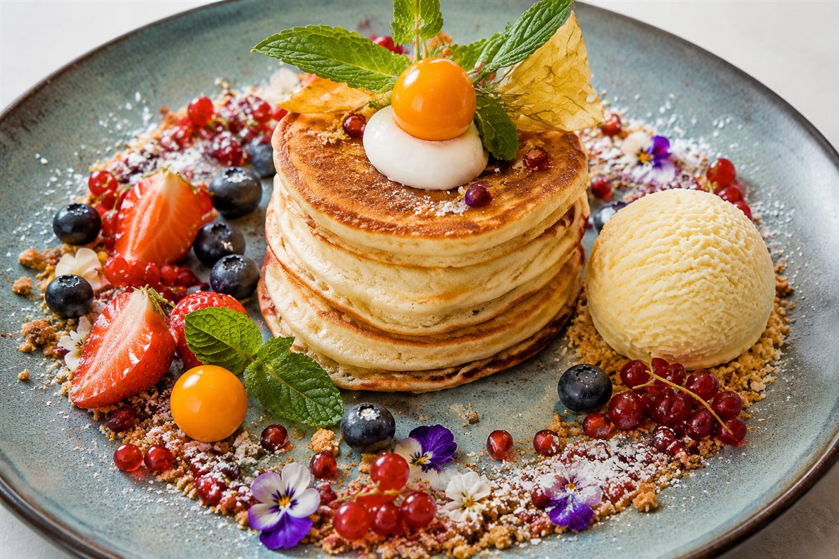 Fluffige Pancakes mit Beeren, Granatapfel, Blüten und einer Kugel Eis
